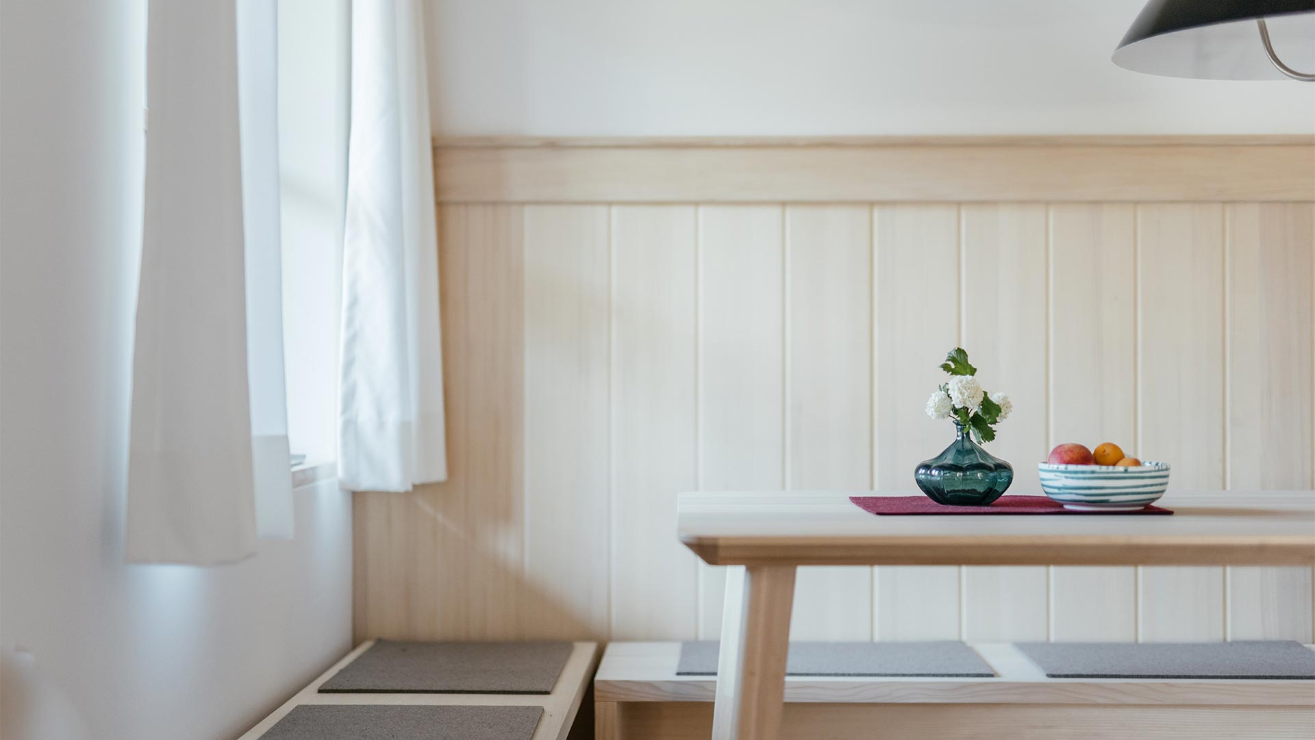 Detailansicht mit Blumenvase und Obstschale auf dem Tisch der stilvollen Sitzecke mit Holzvertäfelung in einer Ferienwohnung im Haus Herzogstand